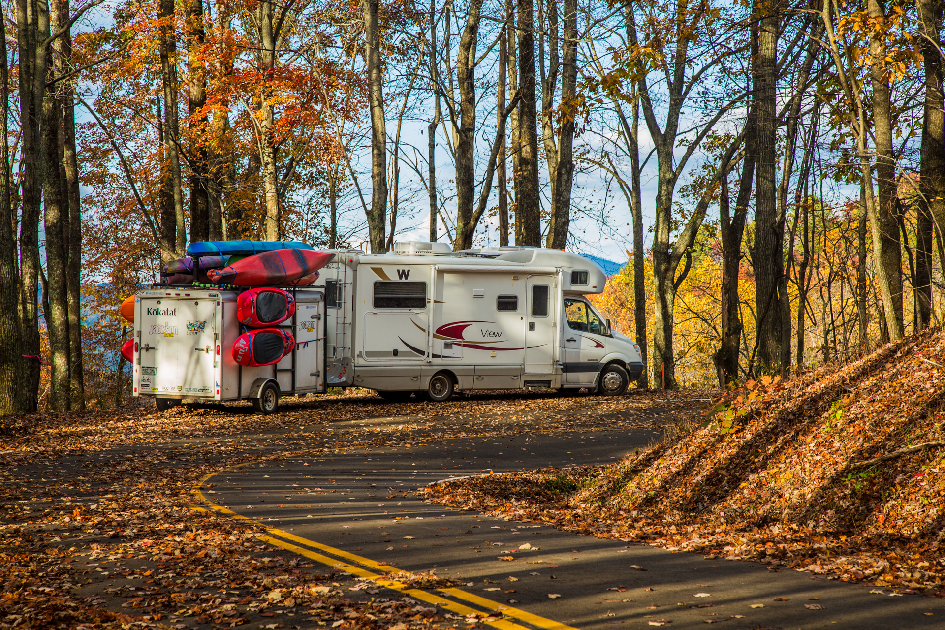 Winnebago View with trailer attached parked along the side of the road among fallen leaves.