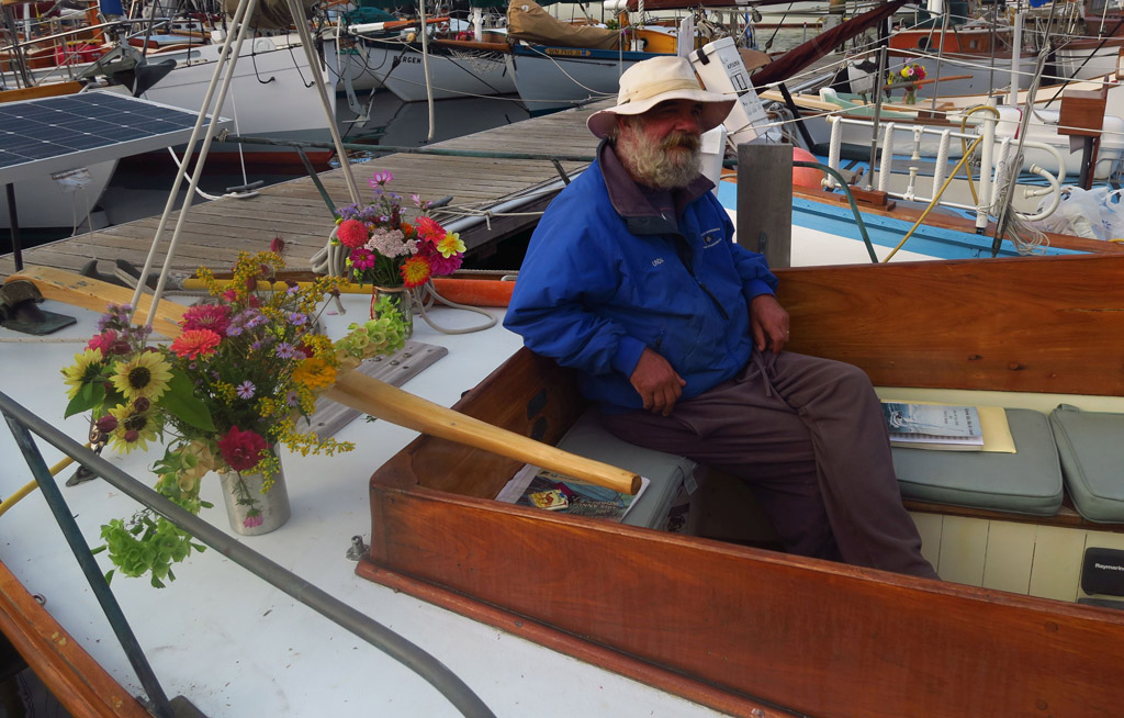 Gentleman sitting at the back of a docked boat with flowers sitting next to him.