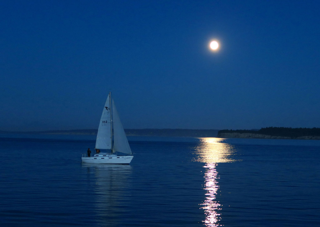 Sailboat on the water with the moon reflecting against the water. 