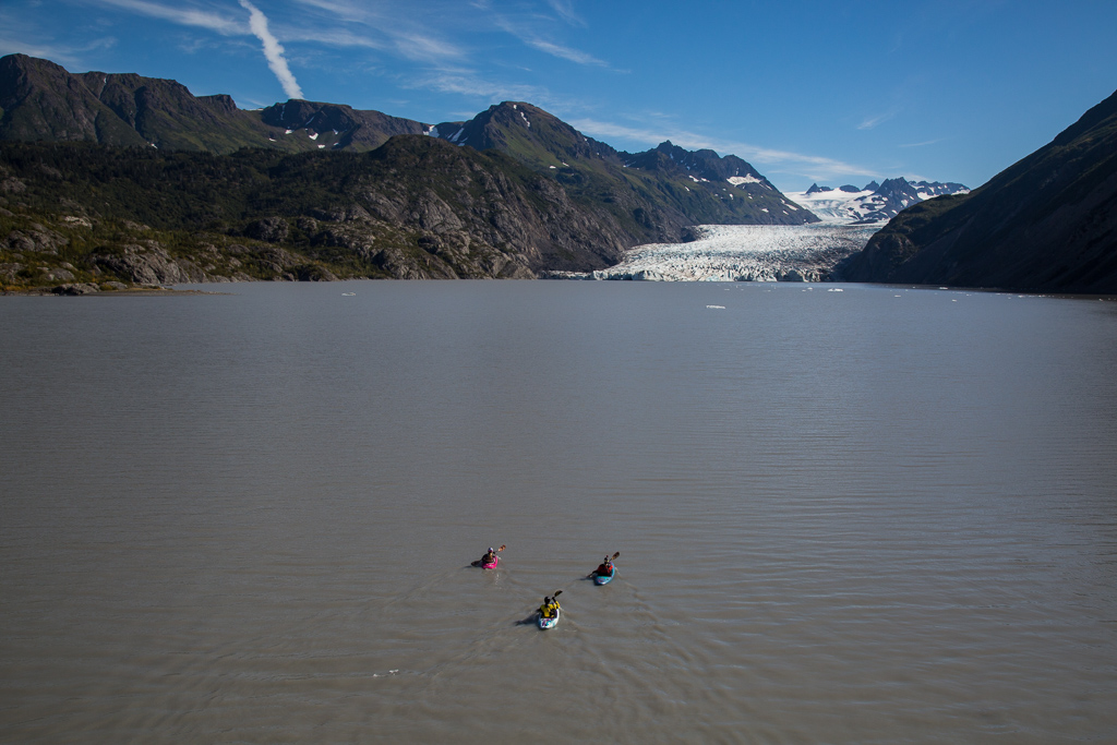 Three kayakers out on glacier lake with glacier ahead.