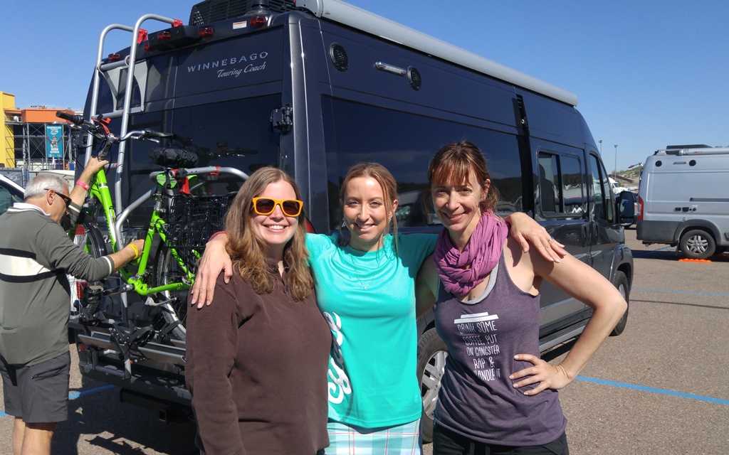 3 women standing outside a Winnebago touring coach.