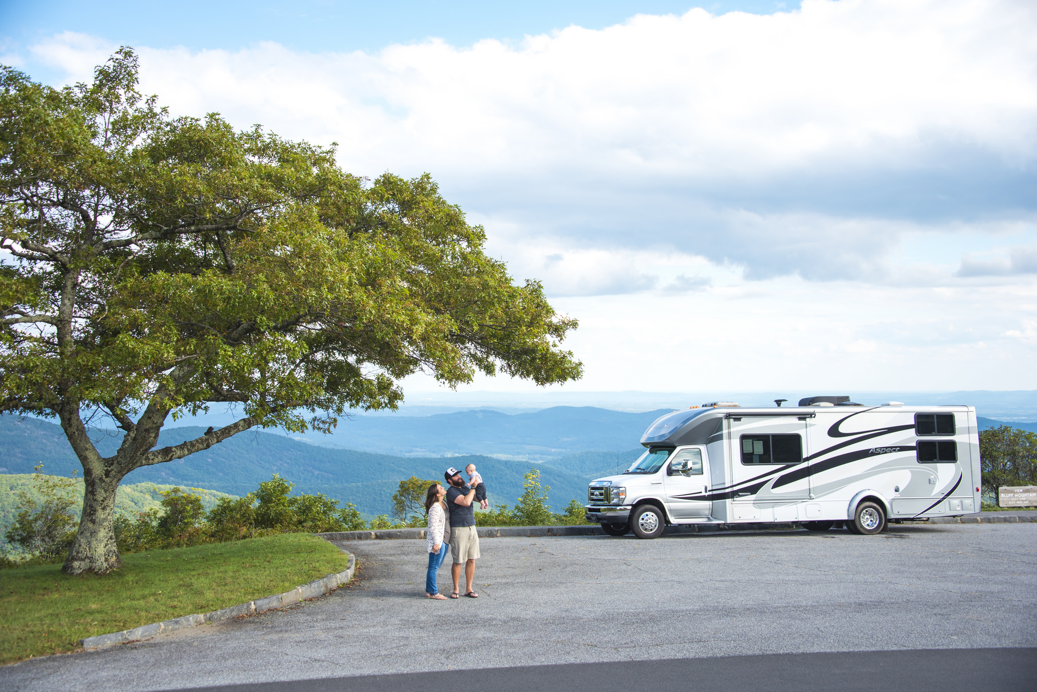 Couple with baby standing in front of their Winnebago Aspect with beautiful scenery around them.