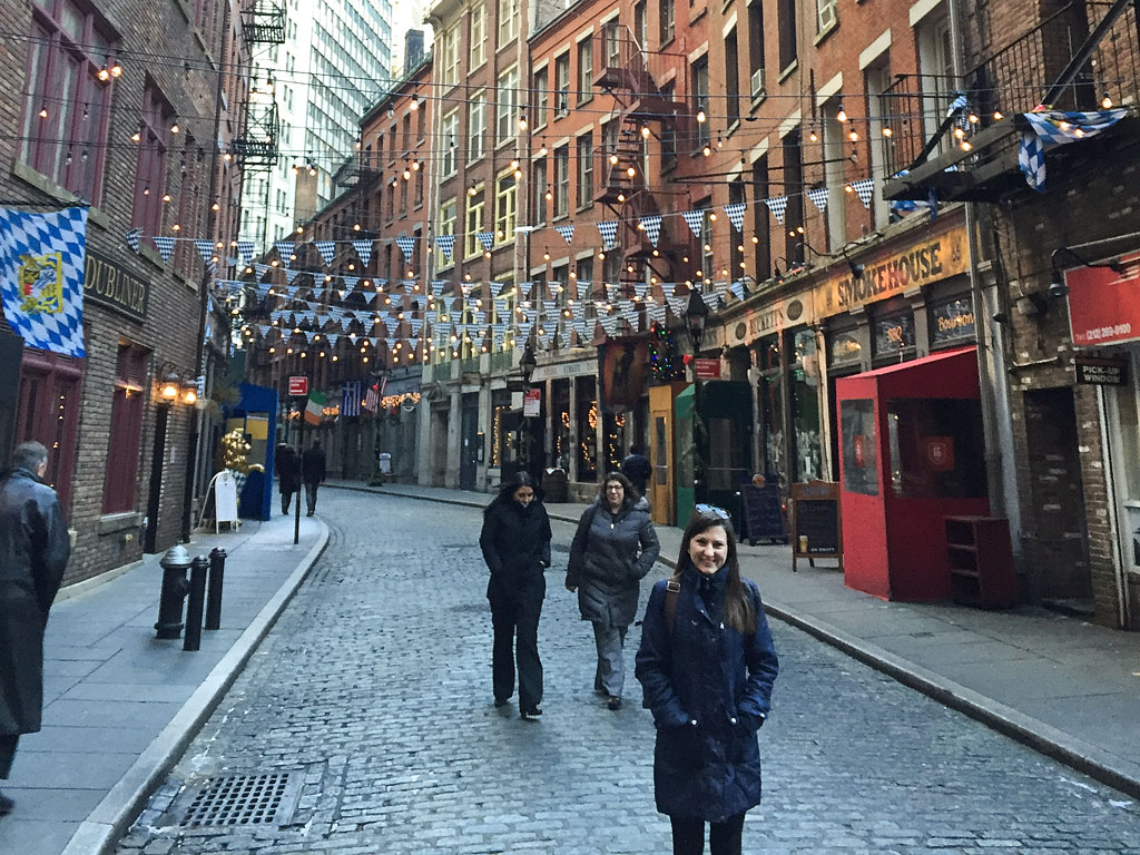 Brittany standing between buildings on Stone Street with lights strung overhead.
