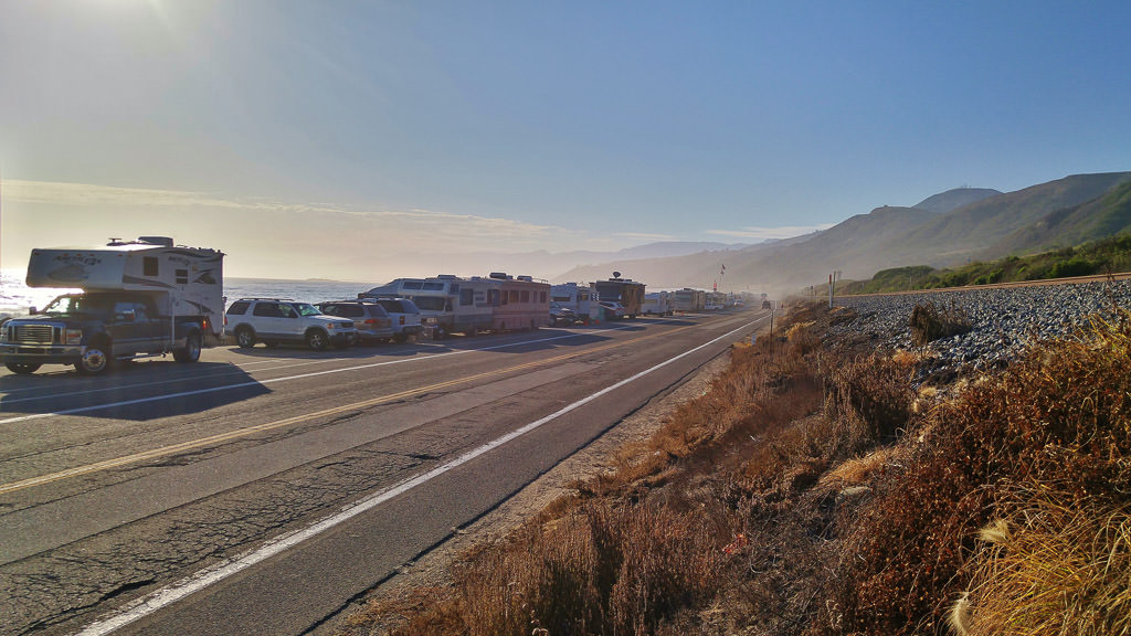 Cars and RVs lining roadway along coastline.