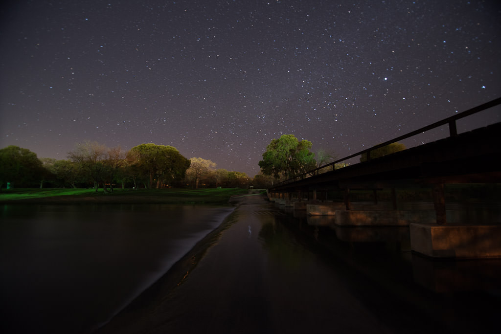 Star-filled night sky above a bridge.