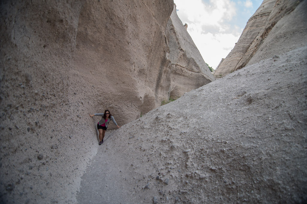 Woman climbing between narrow valley created by large rock formations.