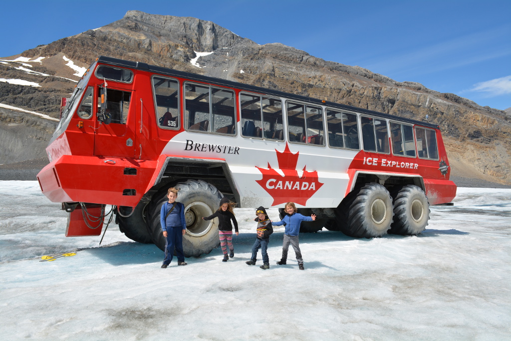 Four kids standing on the glacier outside the Brewster Ice Explorer Truck.