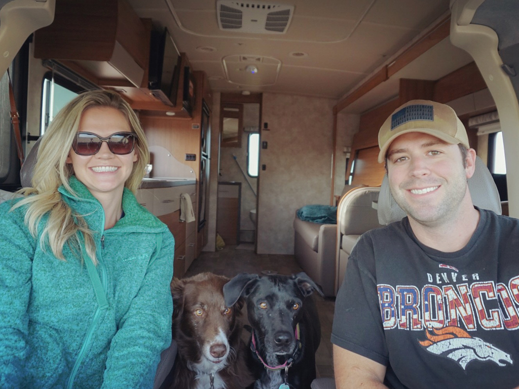 Smiling selfie of Dan and Lindsay and their two dogs in their Winnebago Navion.