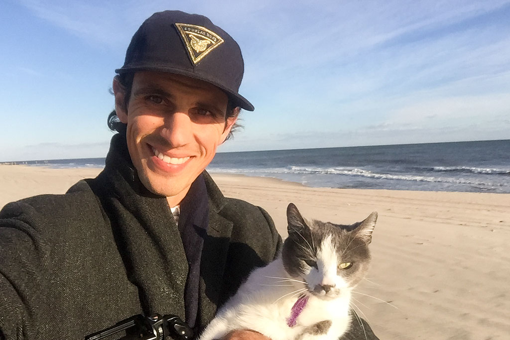 Jordan and their cat standing on the beach with ocean in view