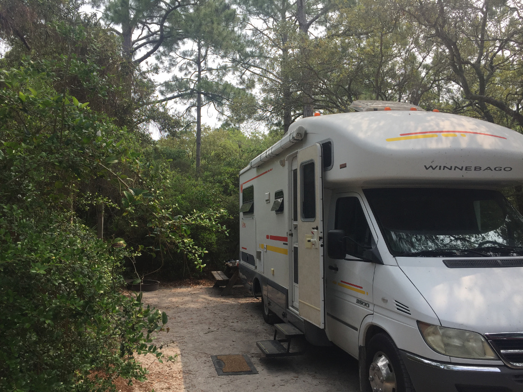 Winnebago RV parked in camp site surrounded by trees