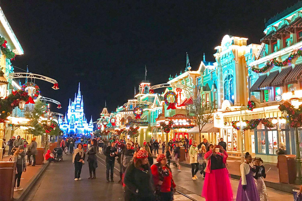 Main walkway in Disney World with castle in background and people dressed for Christmas