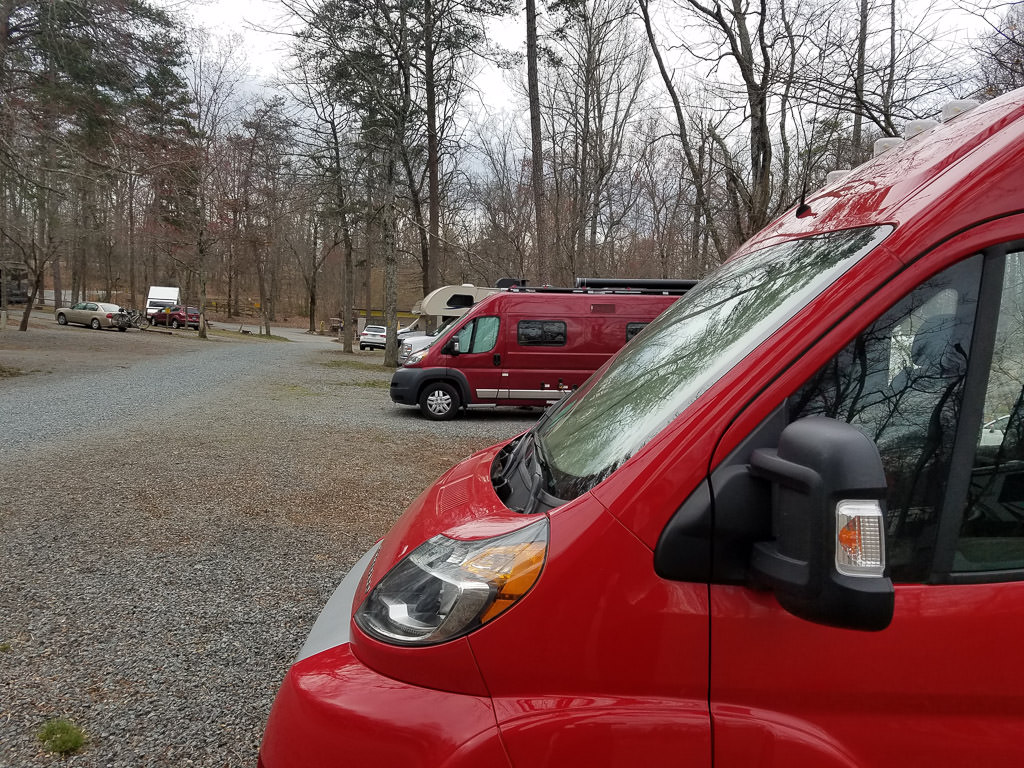 Two red Winnebago Travatos parked at a campground