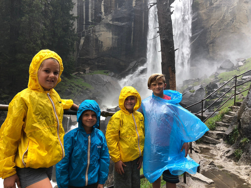4 kids with rain ponchos on standing in front of a waterfall