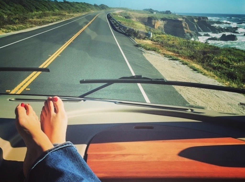 Feet on dash and view of road along the coastline ahead.