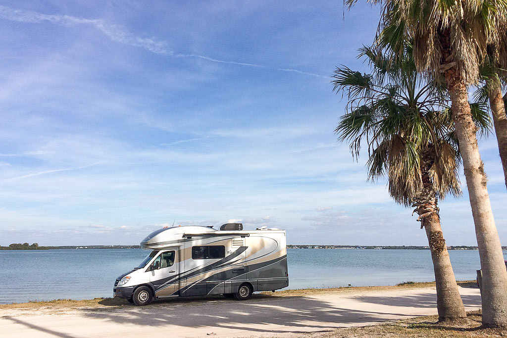 Winnebago View parked next to palm trees with water in the background